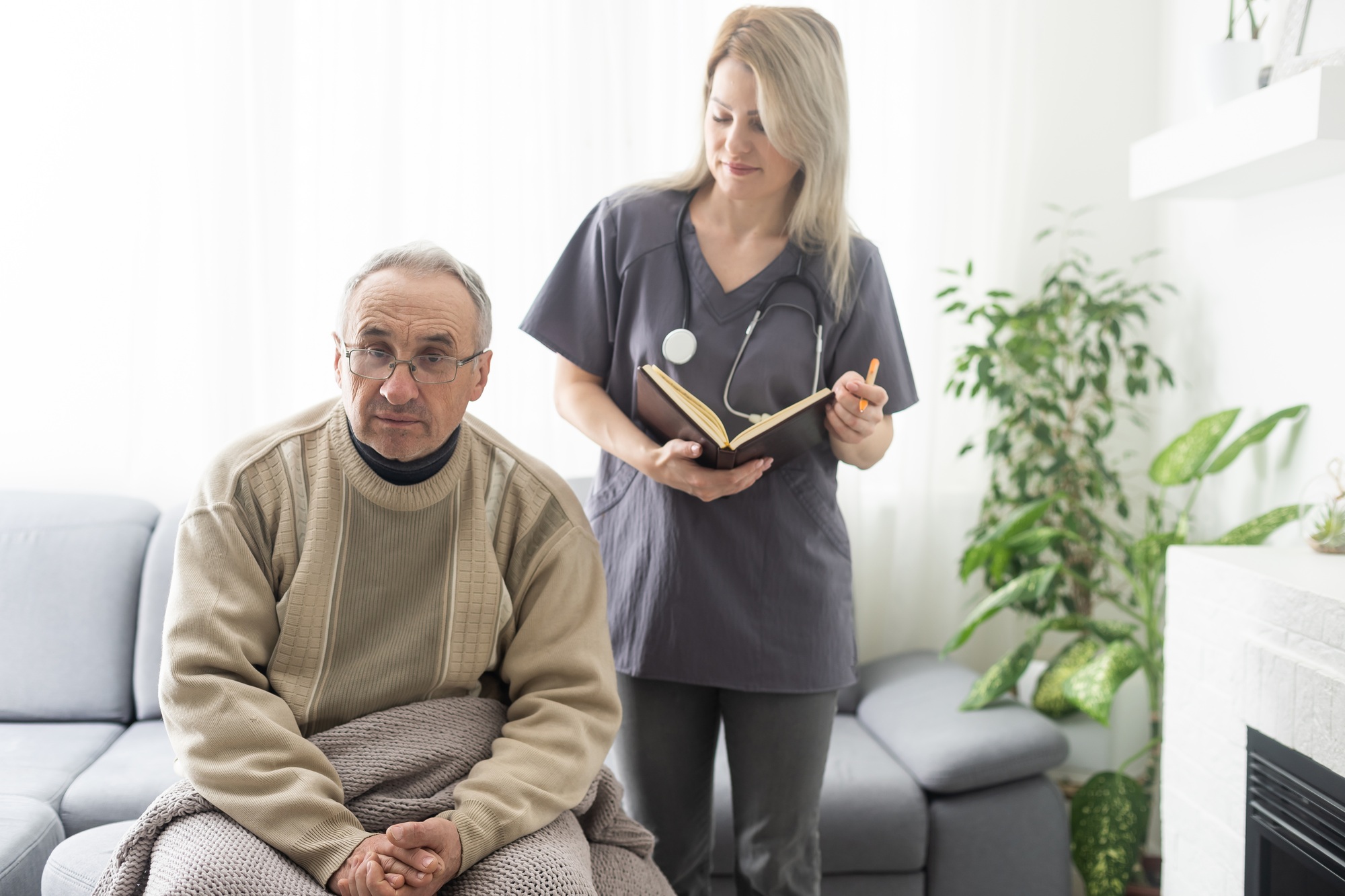 Caring nurse talks to old patient holds his hand sit in living room at homecare visit provide